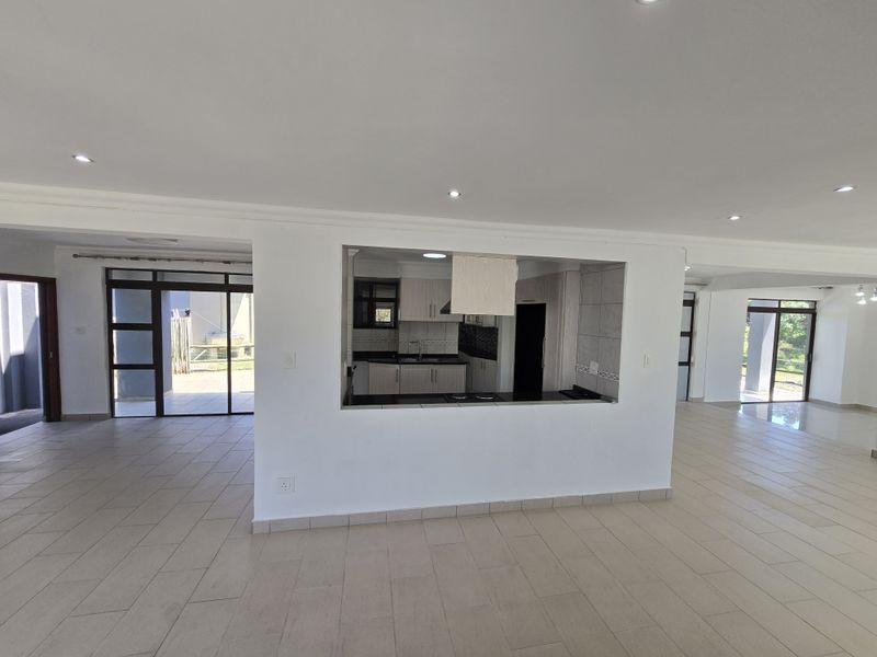 Spacious open-plan living area featuring neutral tiled flooring, recessed lighting, and a functional kitchen pass-through window with built-in cabinetry.