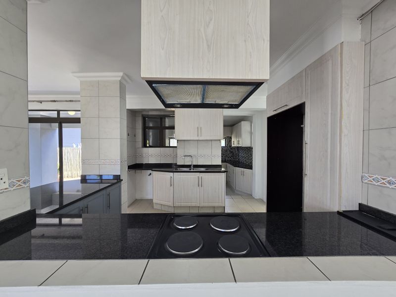 Spacious kitchen featuring built-in cabinetry, granite countertops, an electric hob with extractor fan, and a functional layout with a separate scullery area.