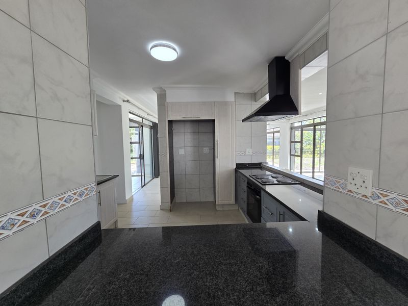 A clean, modern kitchen featuring granite countertops, built-in oven, electric hob, extractor fan, and ample cabinetry, offering a functional and well-maintained cooking space.