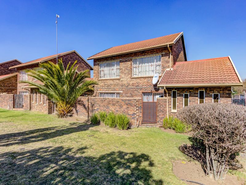 Rear view of a face brick townhouse featuring a tiled roof, security bars on windows, and a private garden area with boundary wall.