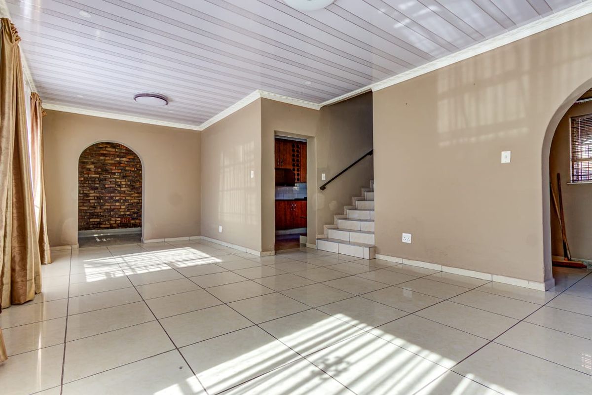 Spacious open-plan living area featuring tiled floors, an exposed brick archway, and a staircase leading to the upper level.