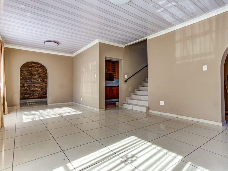Spacious open-plan living area featuring tiled floors, an exposed brick archway, and a staircase leading to the upper level.