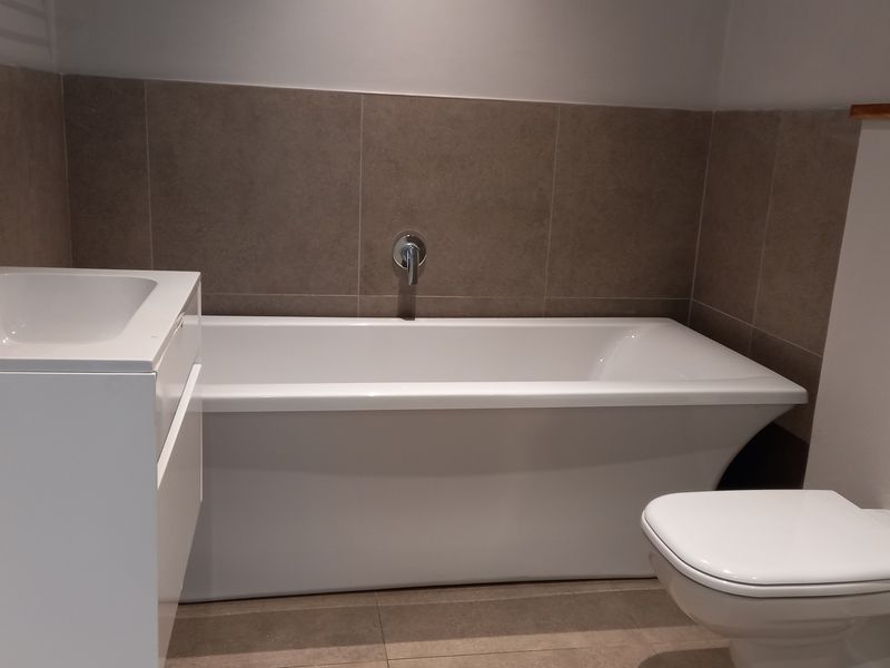 Modern bathroom featuring a sleek bathtub, wall-mounted faucet, vanity basin, and a wall-hung toilet with a concealed cistern flush plate.