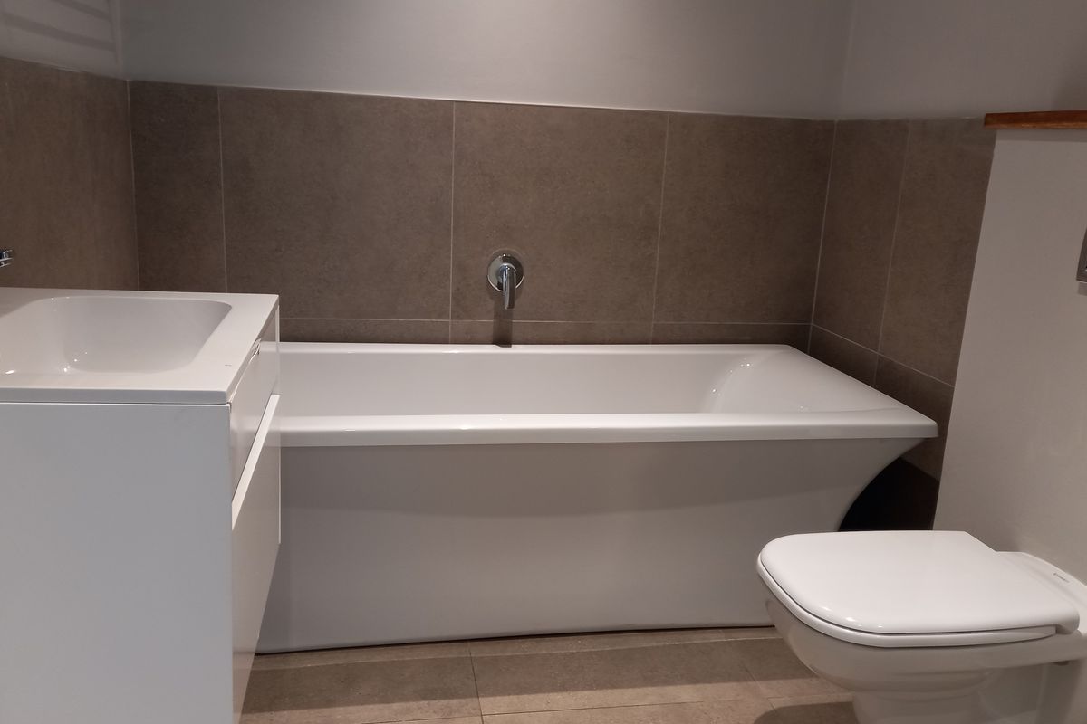 Modern bathroom featuring a sleek bathtub, wall-mounted faucet, vanity basin, and a wall-hung toilet with a concealed cistern flush plate.