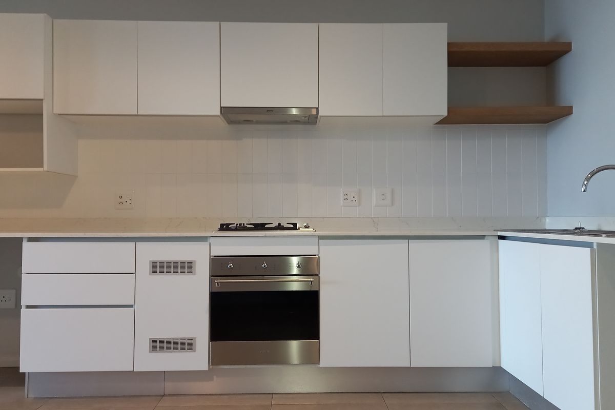 Modern kitchen featuring white cabinetry, stone countertops, a gas hob, built-in oven, extractor fan, and a stainless steel sink with tiled backsplash.