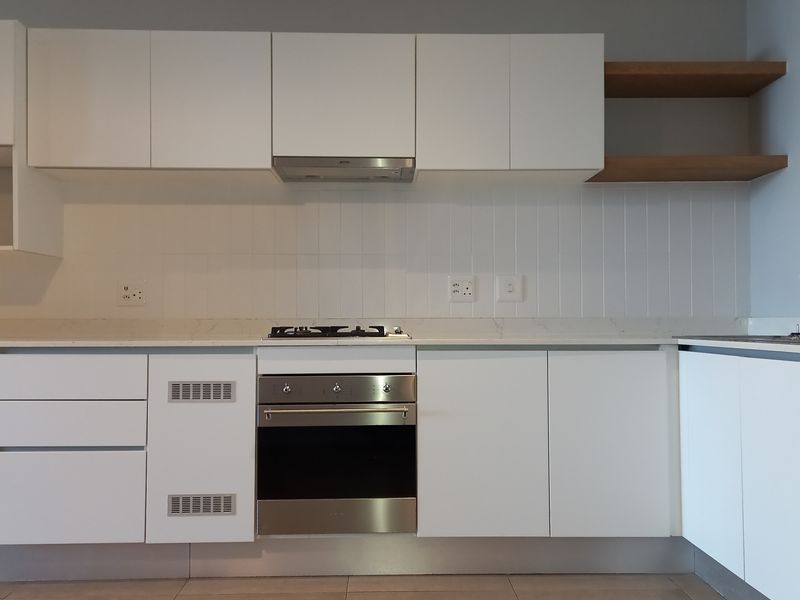 Modern kitchen featuring white cabinetry, stone countertops, a gas hob, built-in oven, extractor fan, and a stainless steel sink with tiled backsplash.