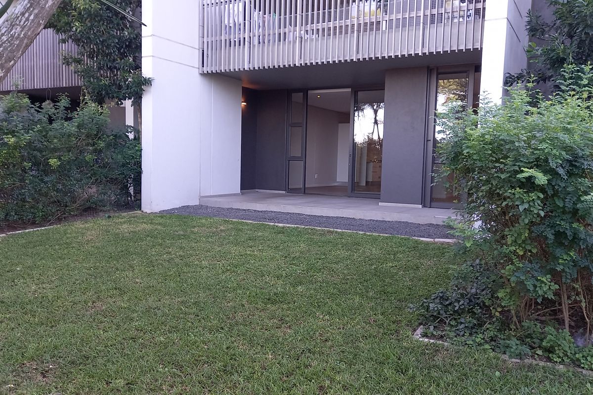 A ground floor apartment featuring a private covered patio with sliding glass doors, overlooking a well-maintained garden area.