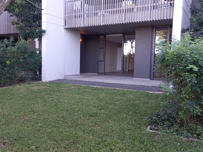 A ground floor apartment featuring a private covered patio with sliding glass doors, overlooking a well-maintained garden area.