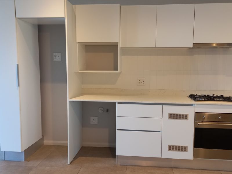 Modern kitchen featuring white cabinetry, stone countertops, integrated gas hob, oven, and extractor fan with neutral tiled flooring.