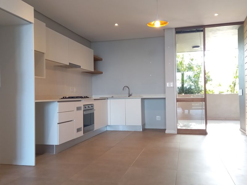 Modern open-plan kitchen featuring sleek white cabinetry, built-in appliances, and tiled flooring, with direct access to a private balcony area.