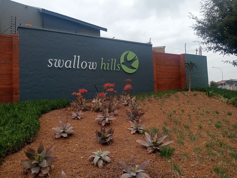 Entrance signage and boundary wall for Swallow Hills estate, featuring well-maintained landscaping and integrated electric security fencing.