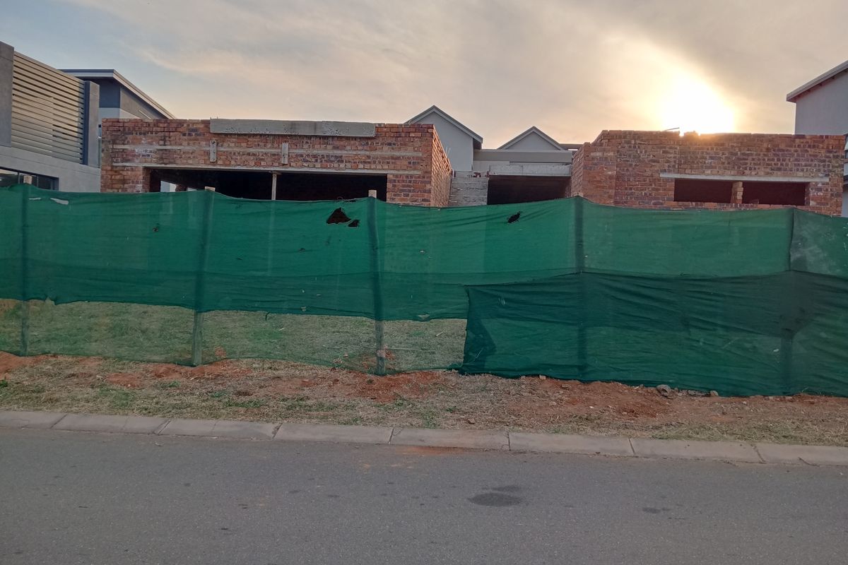 A front view of a residential property currently under construction, featuring exposed brickwork and unfinished structural elements behind a temporary site fence.