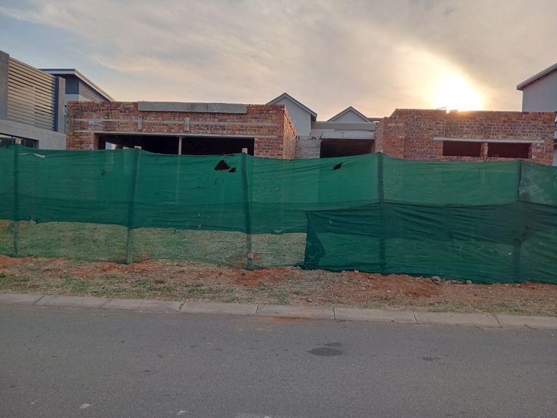 A front view of a residential property currently under construction, featuring exposed brickwork and unfinished structural elements behind a temporary site fence.