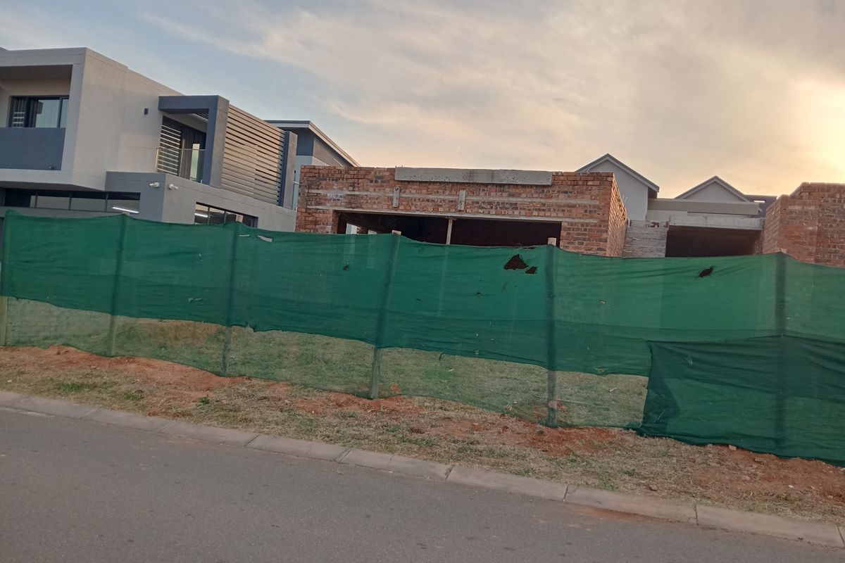 A view of a residential property currently under construction, featuring exposed brickwork and structural elements behind temporary site fencing.