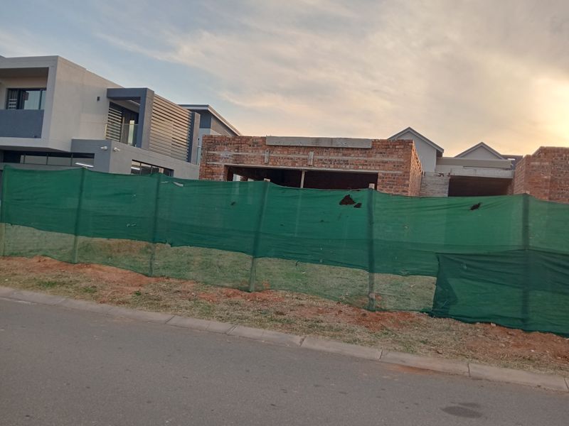 A view of a residential property currently under construction, featuring exposed brickwork and structural elements behind temporary site fencing.