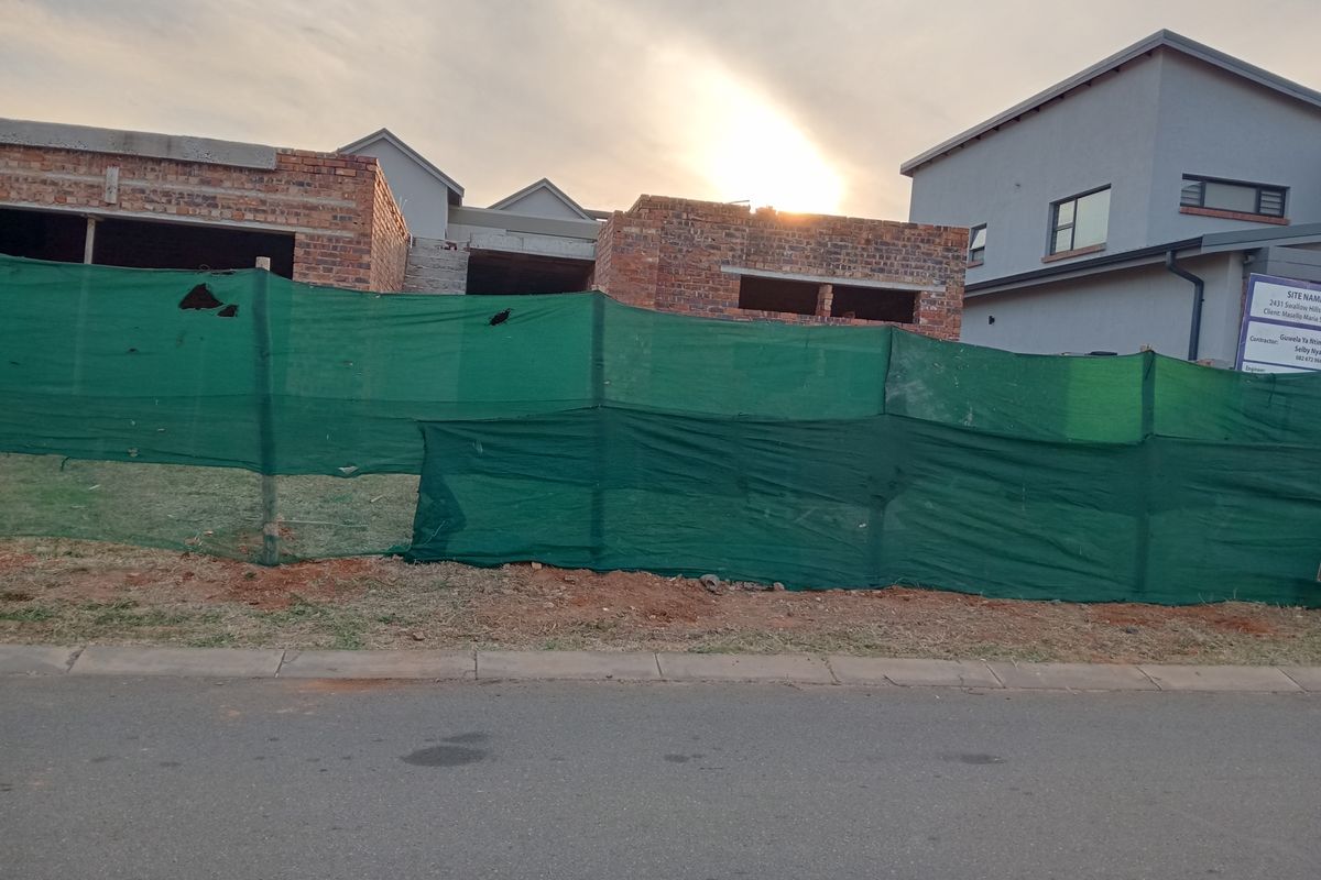 A view of a residential property currently under construction, featuring exposed brickwork and site fencing from the street level.