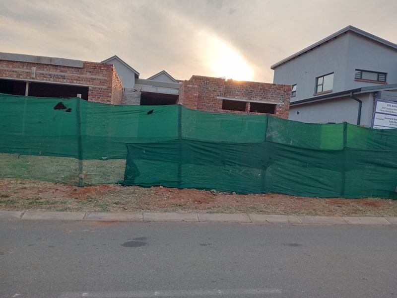 A view of a residential property currently under construction, featuring exposed brickwork and site fencing from the street level.