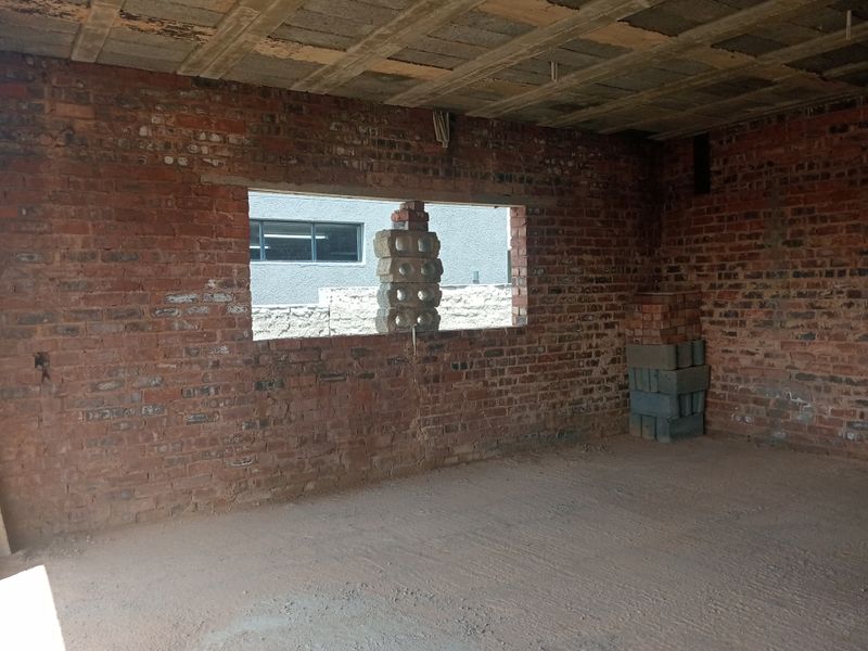 An unfinished interior space featuring exposed brick walls, a raw concrete ceiling, and a concrete floor, currently in the early stages of construction.