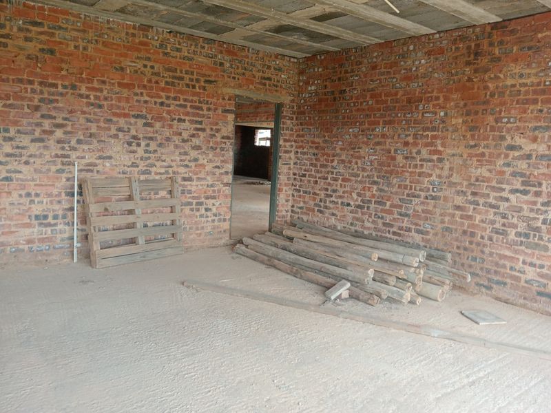 An unfinished interior space featuring exposed brick walls and a raw concrete ceiling, currently in a shell construction state.