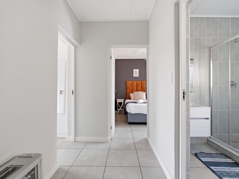 A bright, modern hallway featuring neutral tiled flooring, providing access to a bedroom and a bathroom with a glass-enclosed shower.