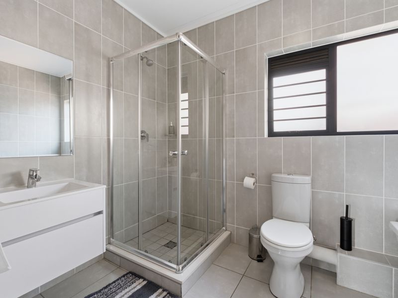 A modern, well-maintained bathroom featuring a glass shower enclosure, a sleek vanity with basin, and neutral floor-to-ceiling wall tiles.