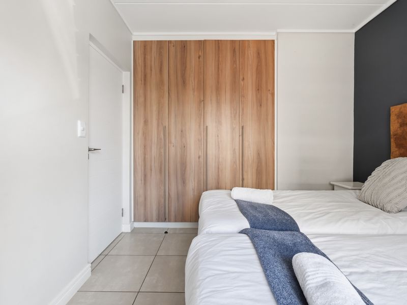 A well-maintained bedroom featuring modern wood-finish built-in cupboards, neutral tiled flooring, and a stylish dark accent wall.
