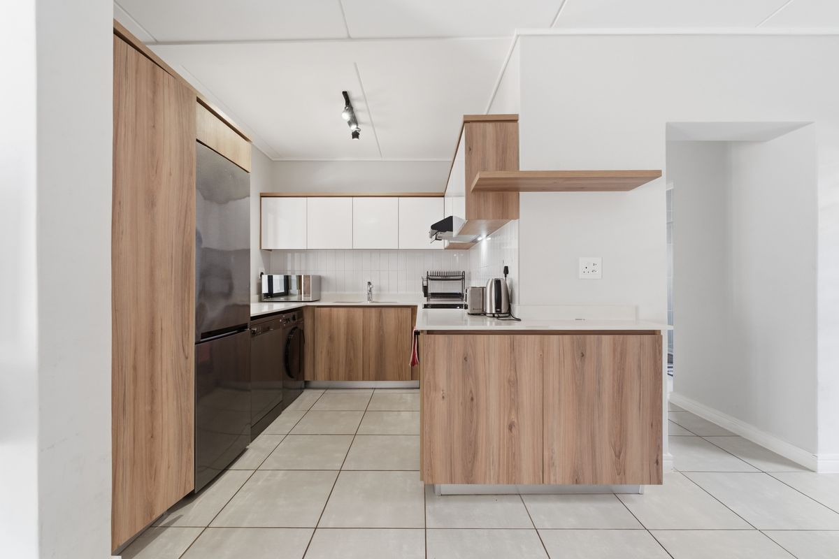 Modern kitchen featuring wood-grain cabinetry, white upper cabinets, tiled flooring, and integrated appliance spaces with clean, contemporary finishes.