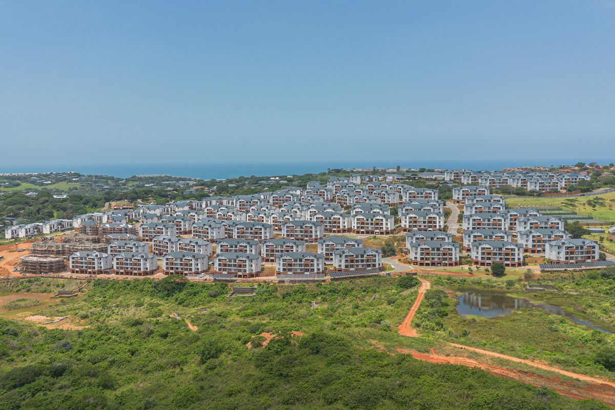 An aerial view of a large residential apartment complex situated in a coastal landscape with surrounding natural vegetation.