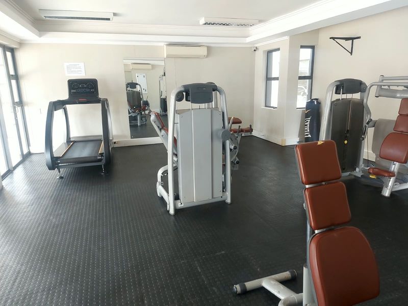 A functional apartment gym facility featuring rubber flooring, wall-mounted mirrors, and integrated air conditioning, equipped with various strength and cardio training machines.