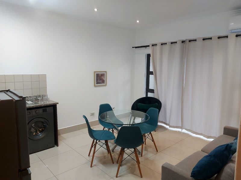 An open-plan living and kitchen area featuring tiled floors, recessed lighting, and a compact kitchen setup with granite countertops and integrated laundry appliance.