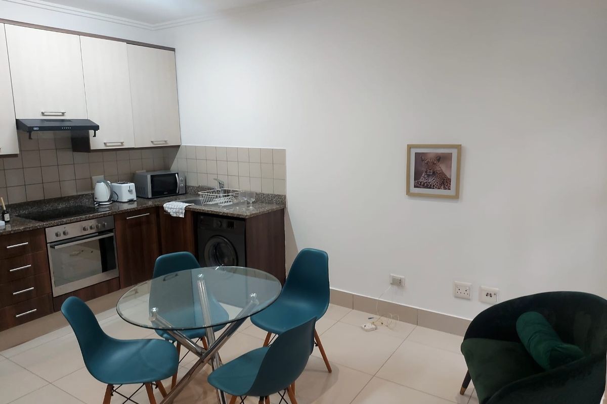 Open-plan kitchen and dining area featuring modern cabinetry, granite countertops, integrated oven and hob, and neutral tiled flooring throughout.