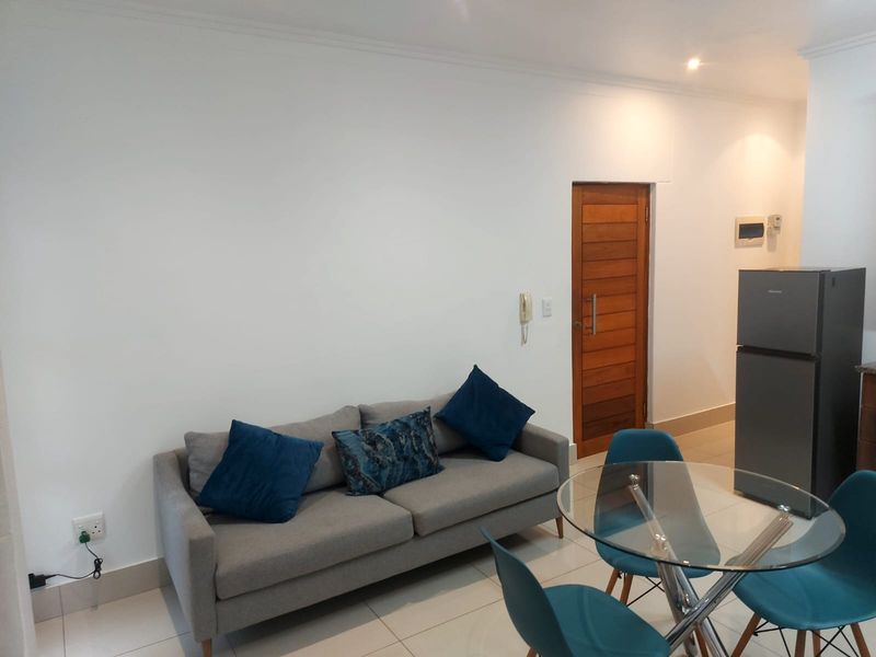 An open-plan living and dining area featuring tiled flooring, a wooden door, and integrated intercom system with neutral wall finishes.