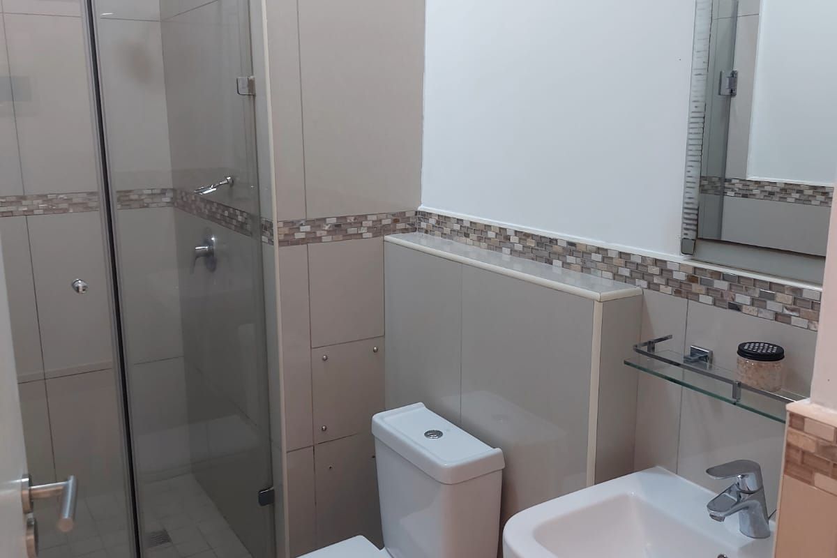 A clean, modern bathroom featuring a glass-enclosed shower, wall-mounted basin, and neutral tiled walls with a decorative mosaic accent border.