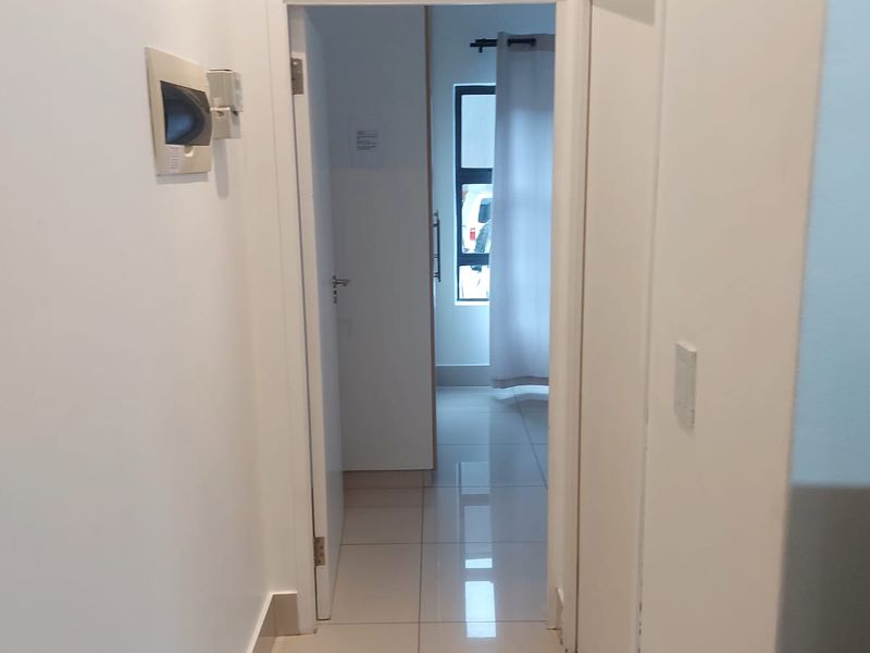 A clean, neutral hallway featuring tiled flooring and access to adjacent rooms, providing a bright and functional transition space within the apartment.