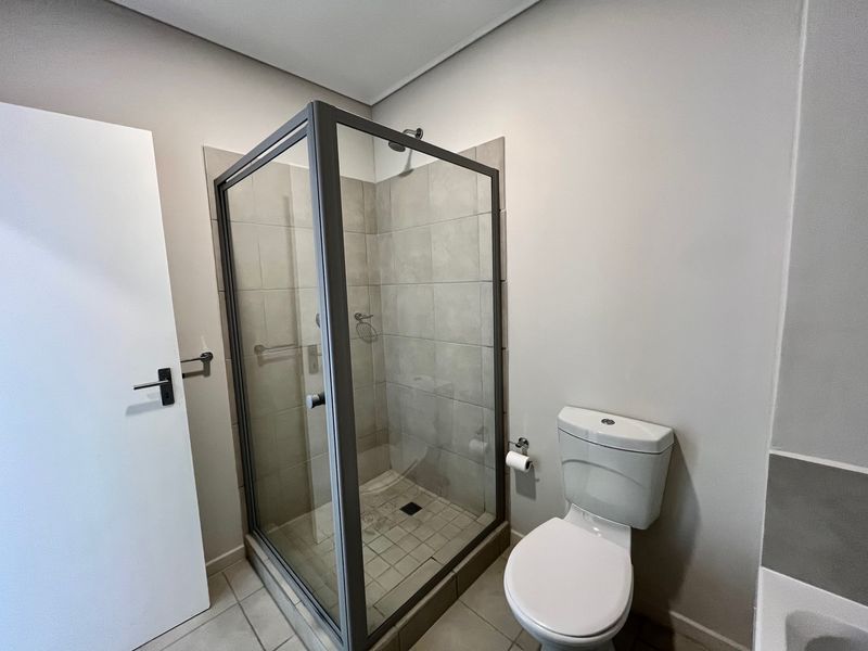 A clean and functional bathroom featuring a glass-enclosed shower, a standard toilet, and neutral floor and wall tiling.