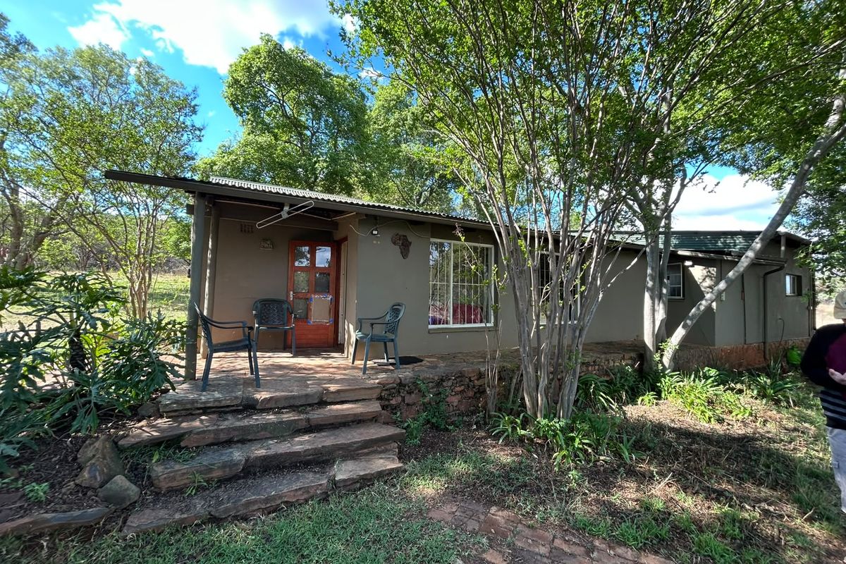 Rear exterior view of a rustic farm cottage featuring a stone patio, stone steps, and mature surrounding trees.
