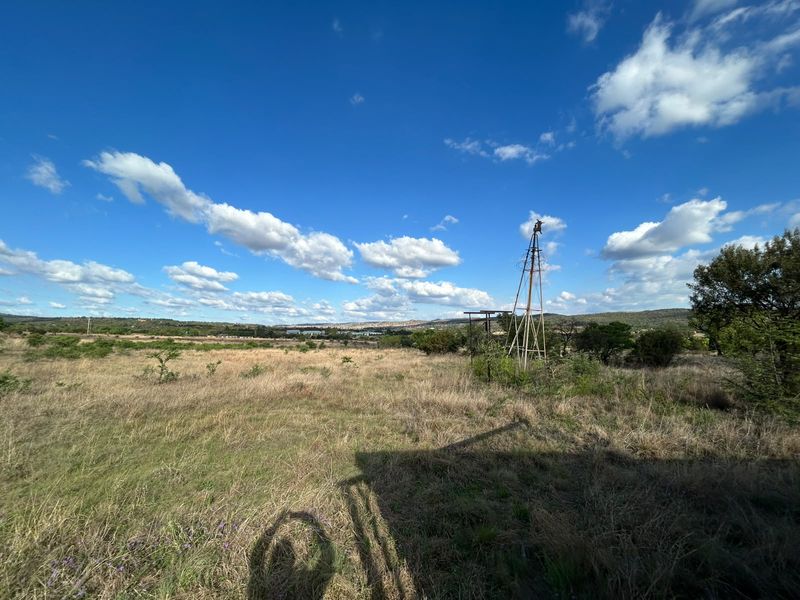 A wide-angle view of the farm landscape featuring an old windmill structure set against a clear blue sky and open fields.