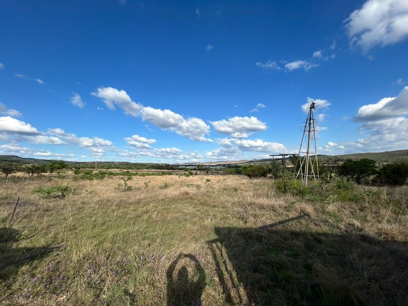 Expansive rural landscape view featuring a traditional metal windmill set within open grassland under a clear blue sky.