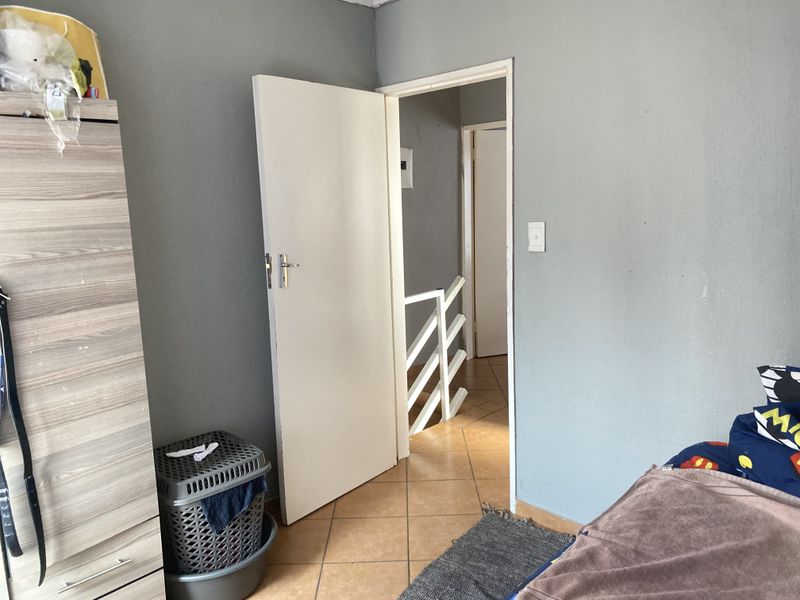 A bedroom featuring tiled flooring and an open doorway leading to a staircase landing area.