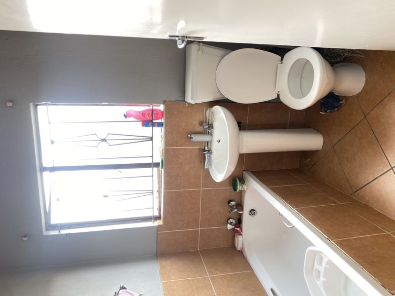 A functional bathroom featuring a pedestal basin, bathtub, and toilet with tiled finishes and a window with security bars.