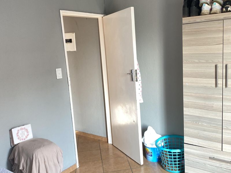 A bedroom featuring tiled flooring, a built-in cupboard, and neutral grey walls, providing a functional space with potential for cosmetic updates.
