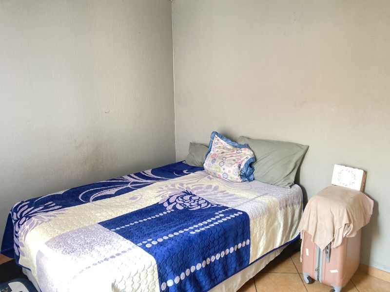 A simple bedroom featuring tiled flooring and plain painted walls, offering a functional space ready for personalization.