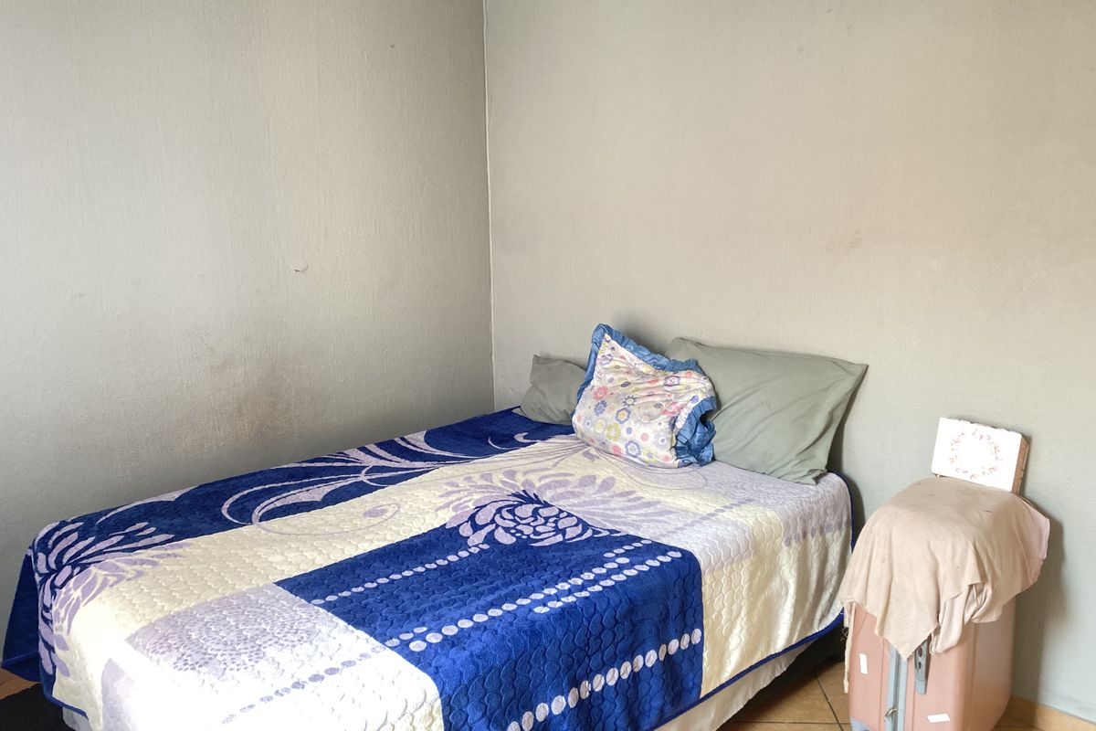 A simple bedroom featuring tiled flooring and plain painted walls, offering a functional space ready for personalization.