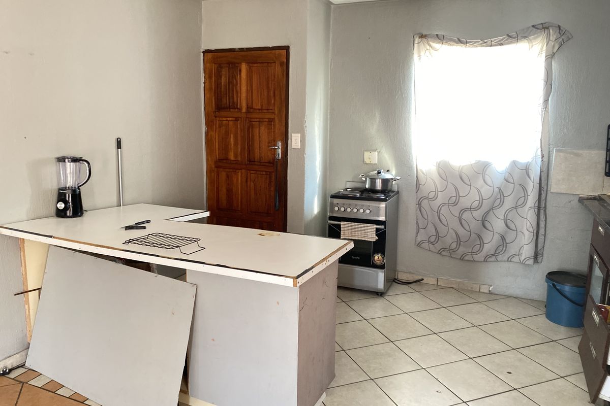 A functional kitchen space featuring tiled flooring, a freestanding stove, and a central island, requiring cosmetic updates to improve its overall condition.
