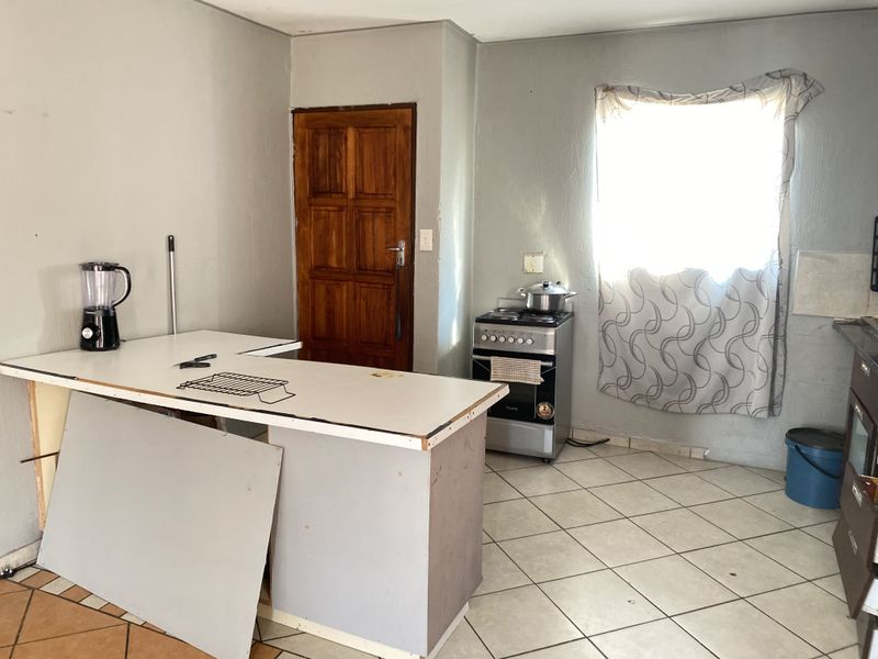 A functional kitchen space featuring tiled flooring, a freestanding stove, and a central island, requiring cosmetic updates to improve its overall condition.