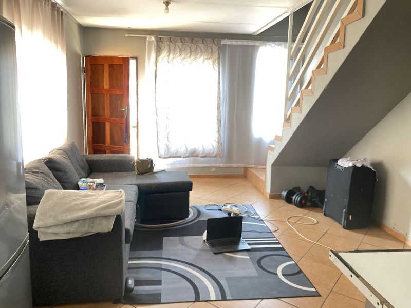 A living room area featuring tiled flooring and an internal staircase, providing access to the upper level of the home.