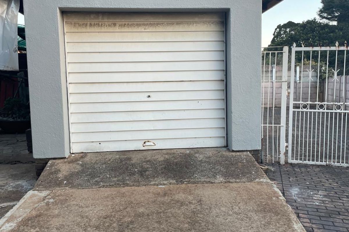 A detached garage featuring a white sectional door, exterior lighting, and a concrete driveway with an adjacent metal security gate.