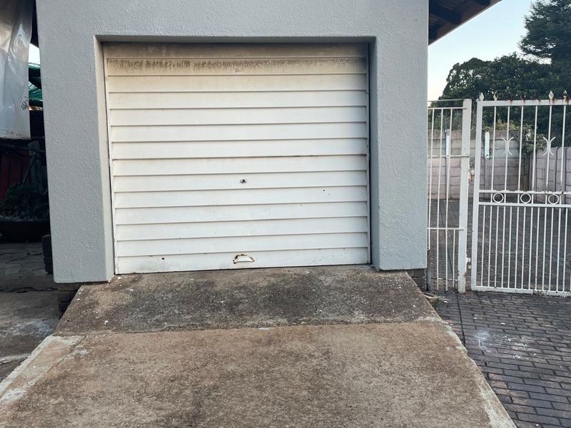 A detached garage featuring a white sectional door, exterior lighting, and a concrete driveway with an adjacent metal security gate.