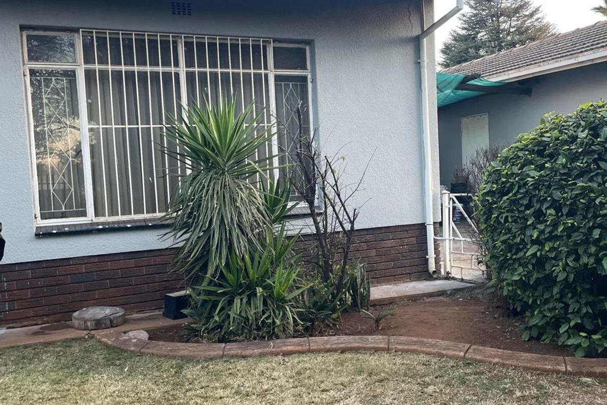 Rear exterior view of the house featuring a tiled roof, brick plinth, and security bars on the windows, set against a garden area.