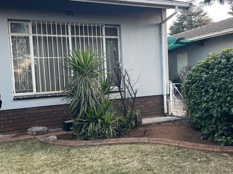 Rear exterior view of the house featuring a tiled roof, brick plinth, and security bars on the windows, set against a garden area.